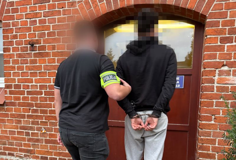 policjant prowadzi sprawcę w kajdankach